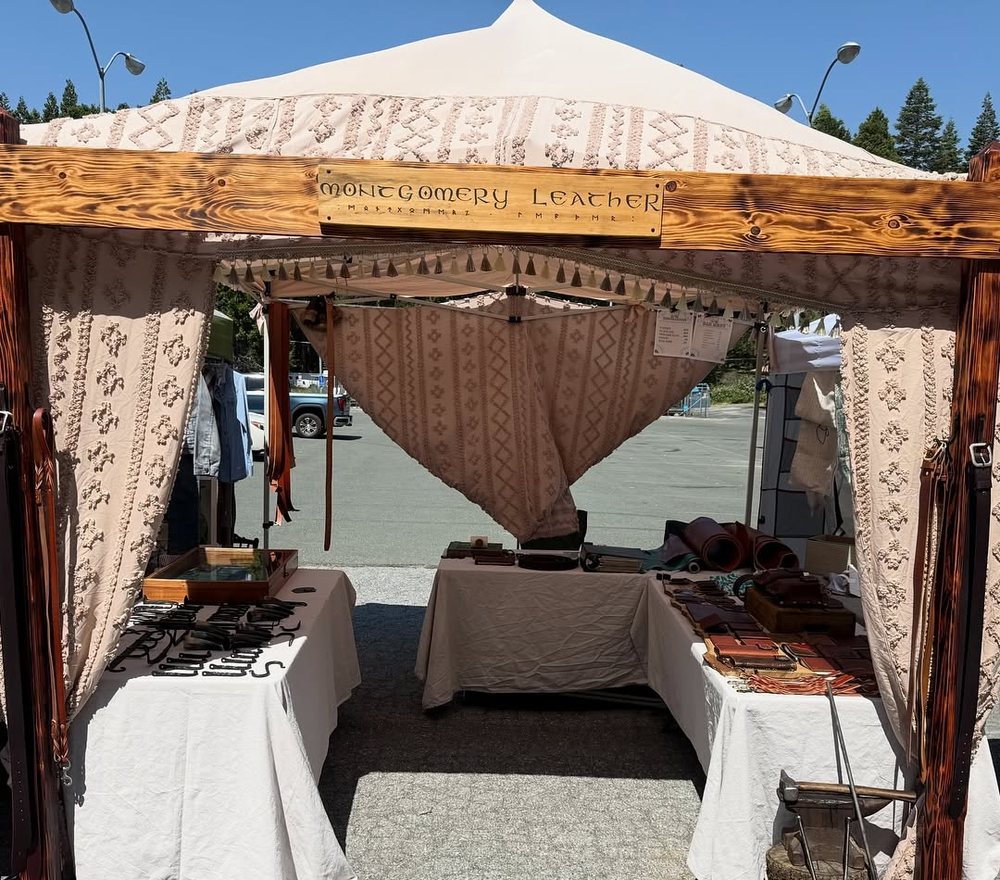 The Montgomery Leather market booth under a white canopy, tables dressed and stock laid out