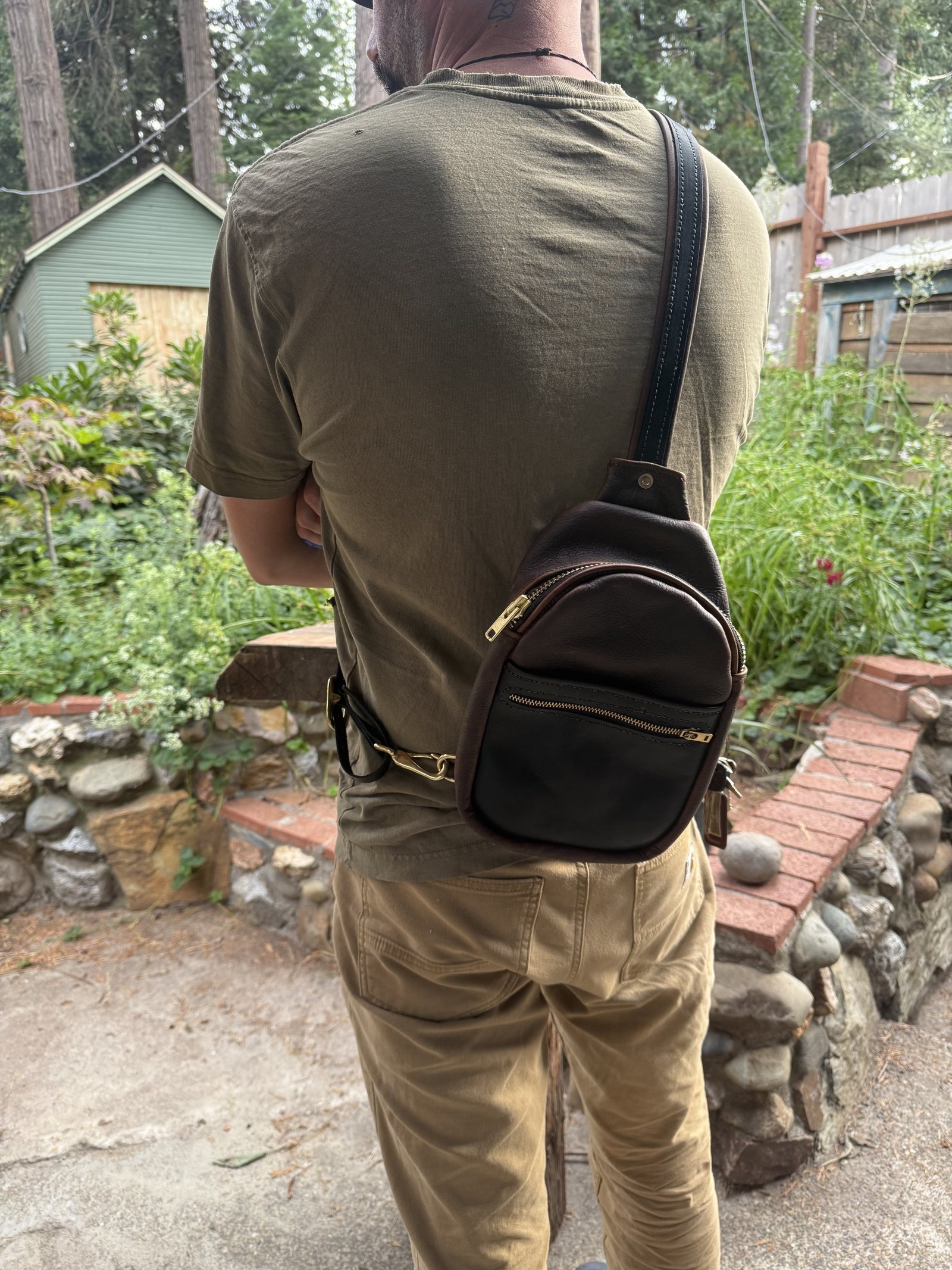 A dark brown leather sling bag worn across the back, its single strap running over one shoulder