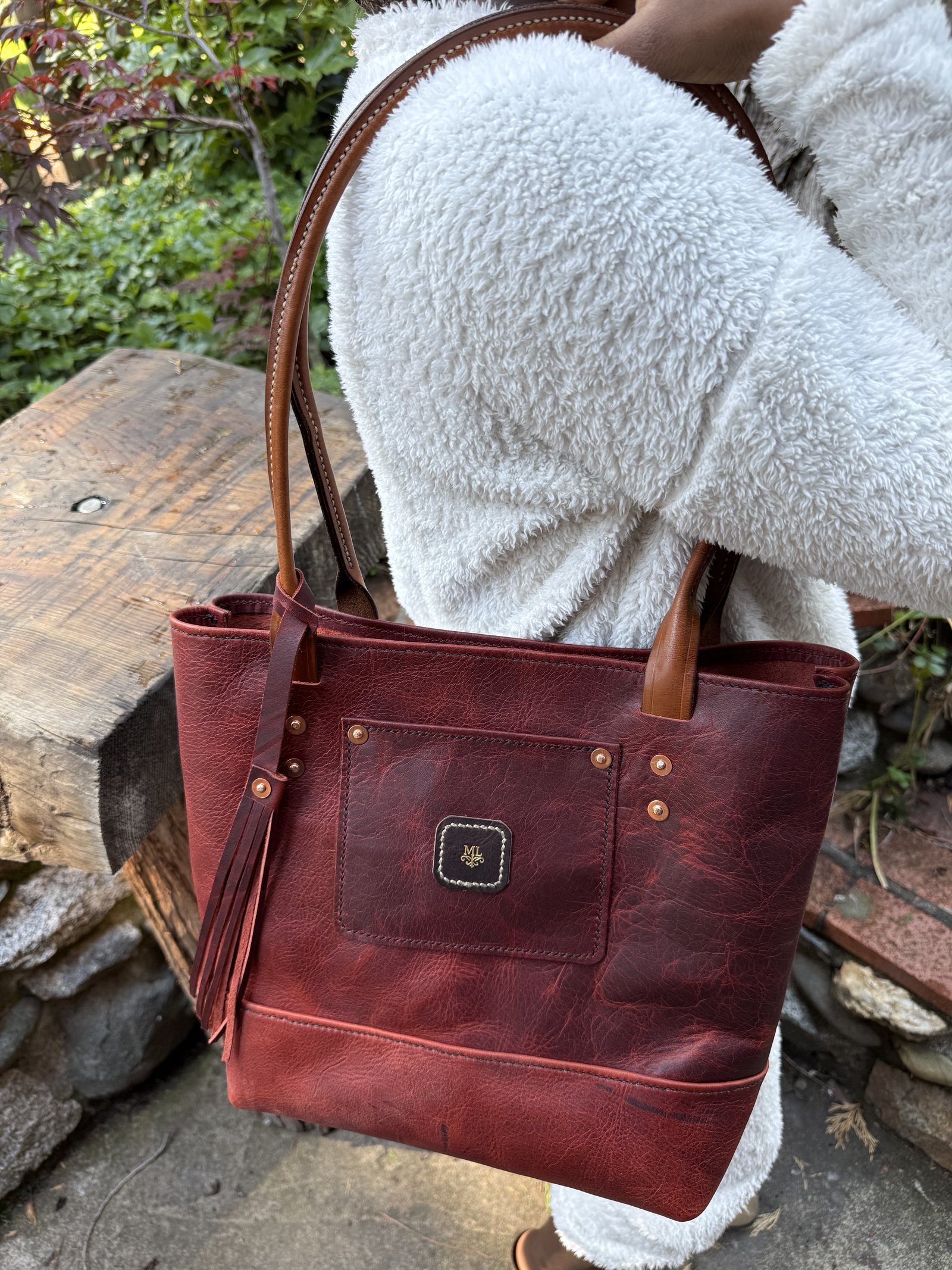 The same red-brown tote carried on the shoulder, its handles long enough to sit over a heavy fleece